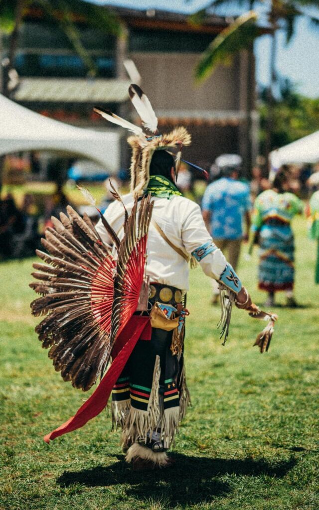 Native American adult man seen from behind, wearing a stunning traditional outfit at the powwow